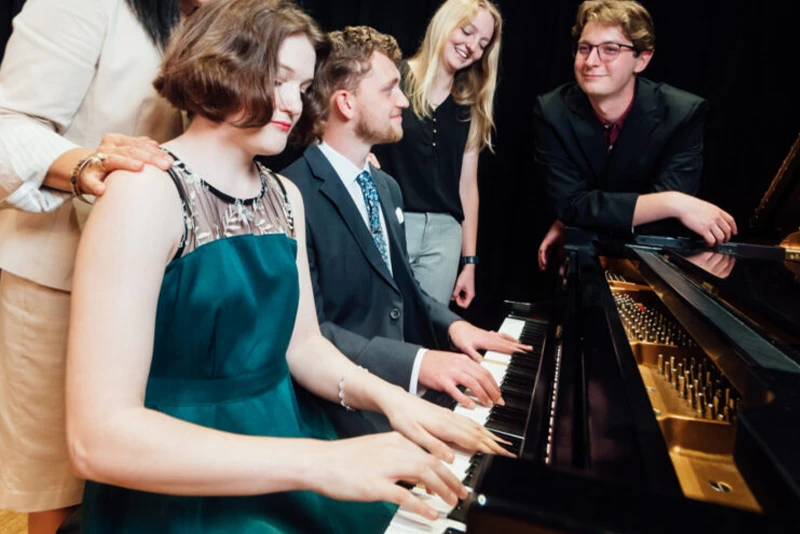 people playing and standing over a piano